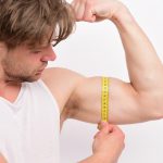 man measuring his bicep with a tape measure