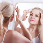 middle age woman looking at her face in mirror