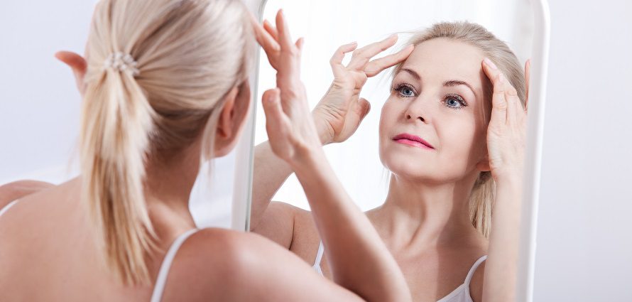 middle age woman looking at her face in mirror